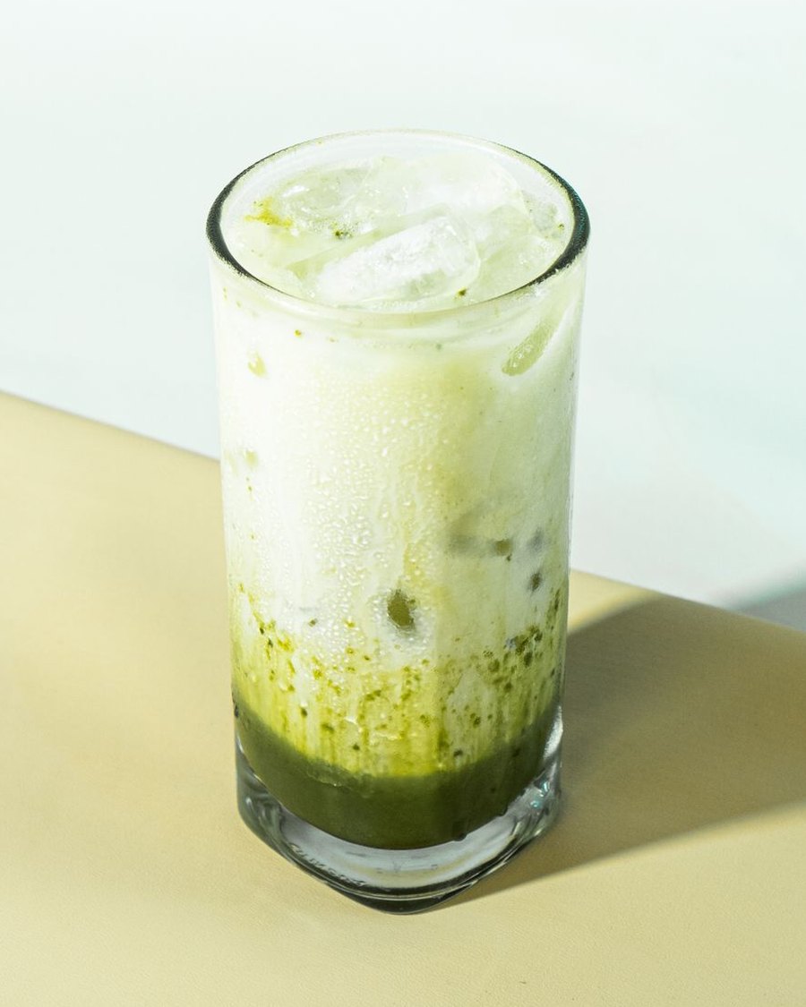 Iskall grön matcha latte med mjölk och is i ett högt glas